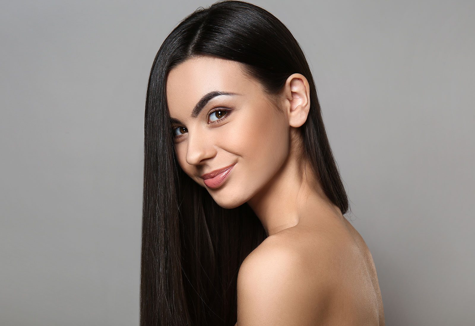 Young adult woman looking over her bare shoulder with long dark hair