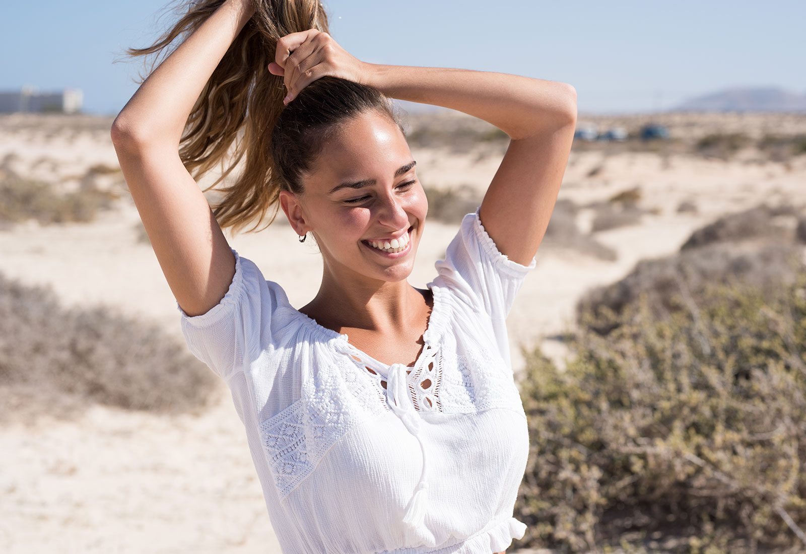 A young adult woman on the beach pulling her hair into a ponytail